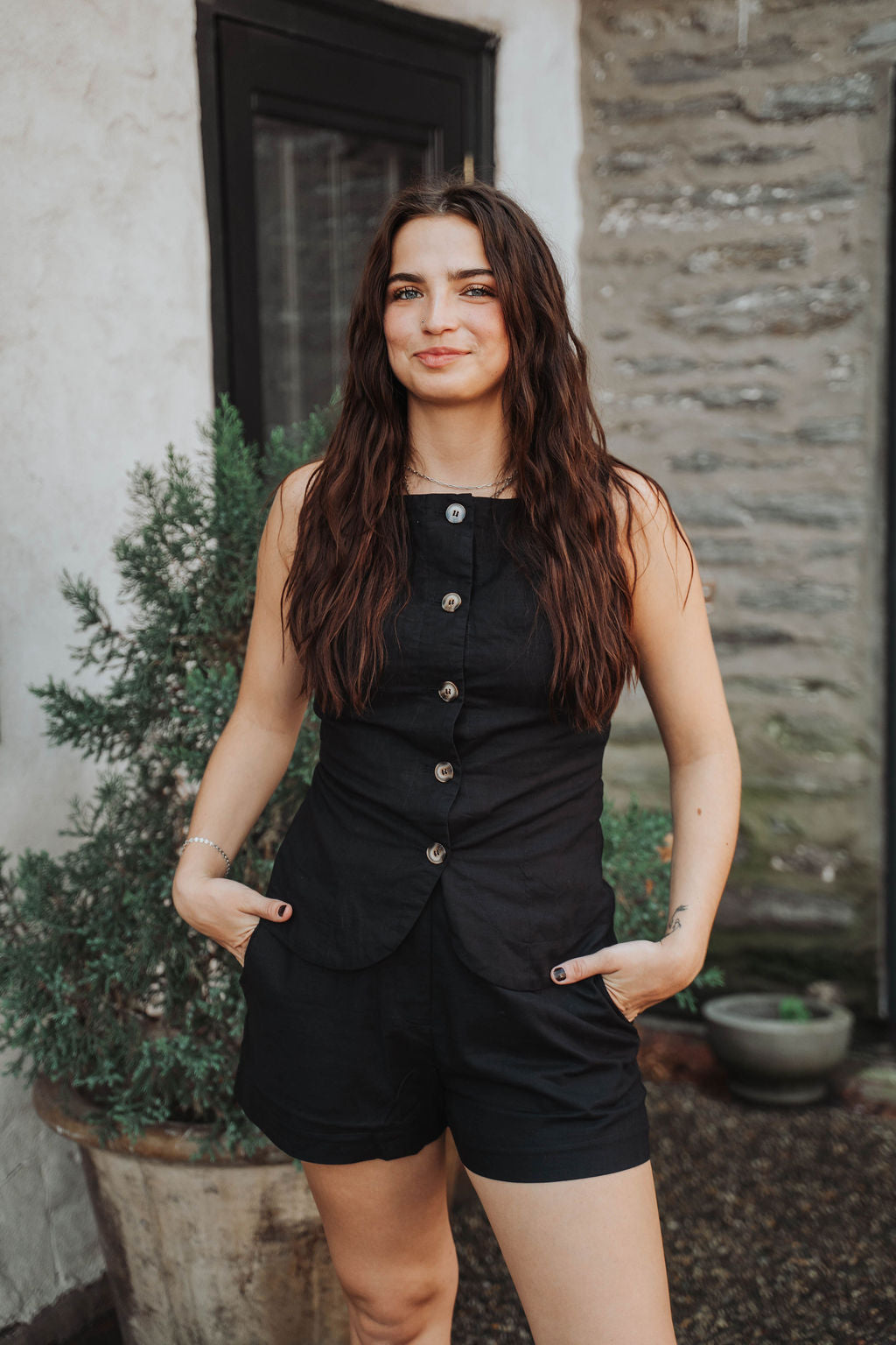 Woman wearing a black sleeveless button-up dress standing outdoors.