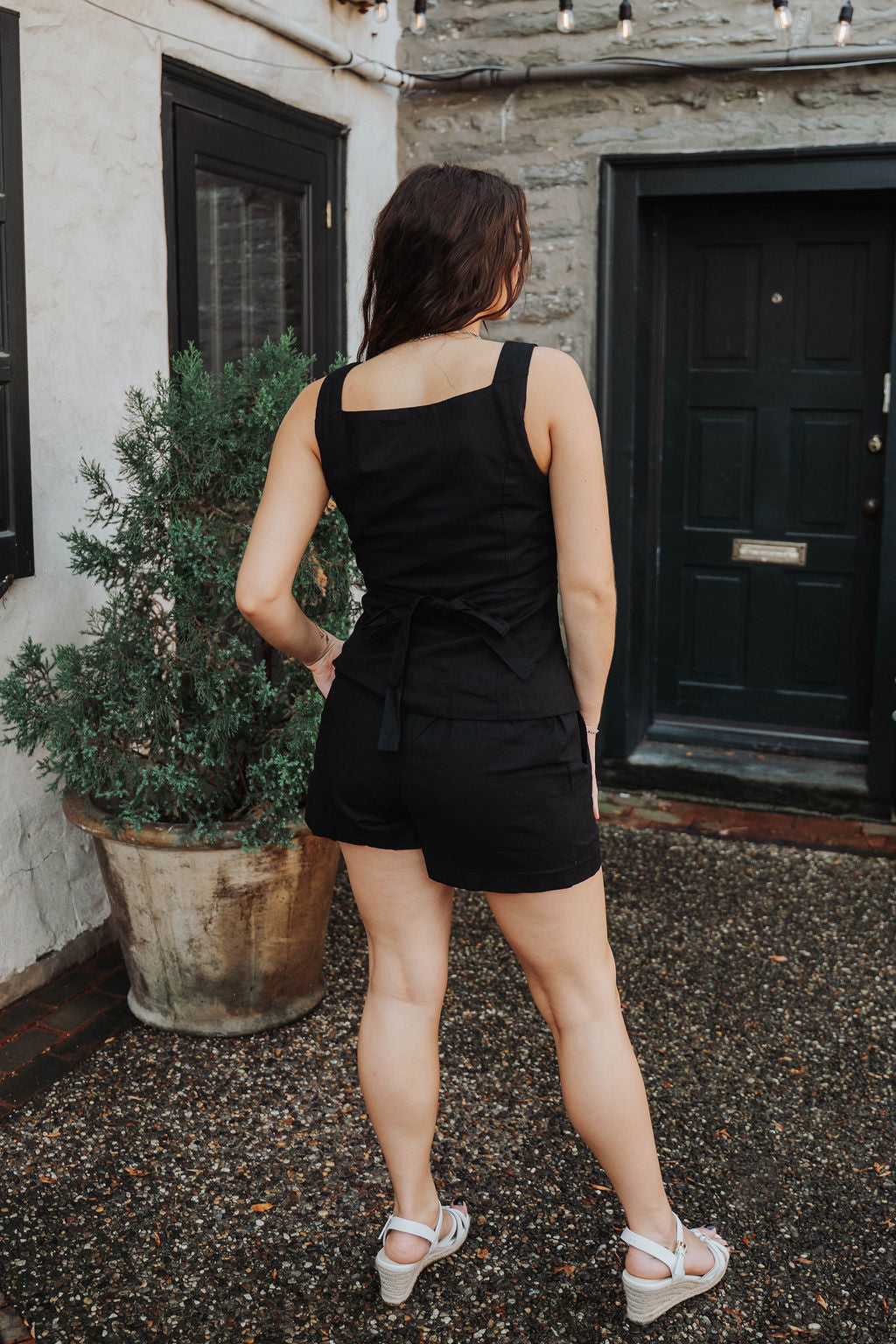 Woman in a black outfit standing in front of a building with a door and plant.