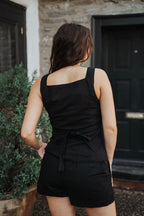 Model wearing a black sleeveless top and shorts standing in front of a building , clothing boutique 