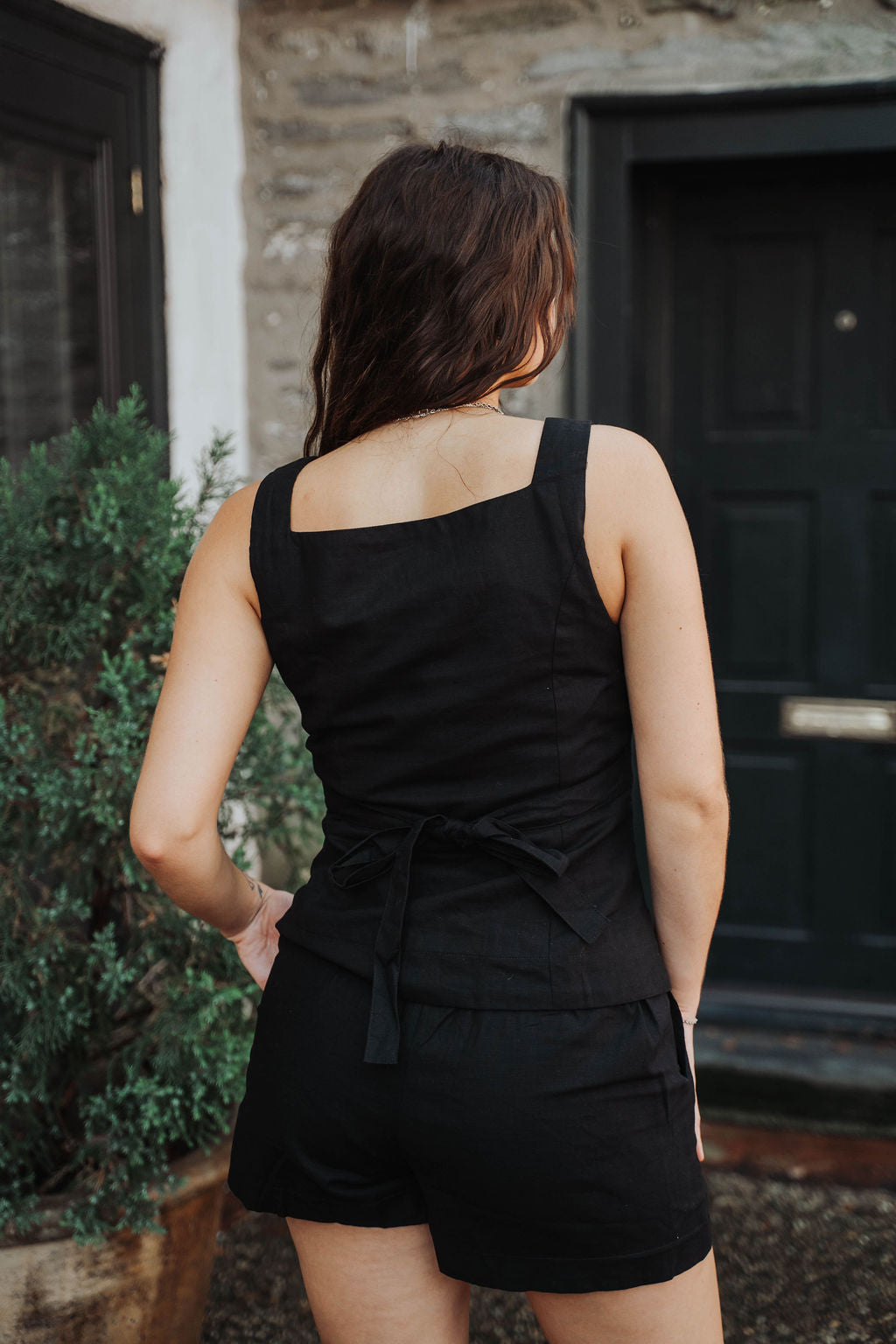 Model wearing a black sleeveless top and shorts standing in front of a building , clothing boutique 