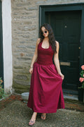 Woman wearing The Juliette Dress – Merlot, a halter maxi with ruched bodice and full gathered skirt in deep wine color, styled with strappy heels.